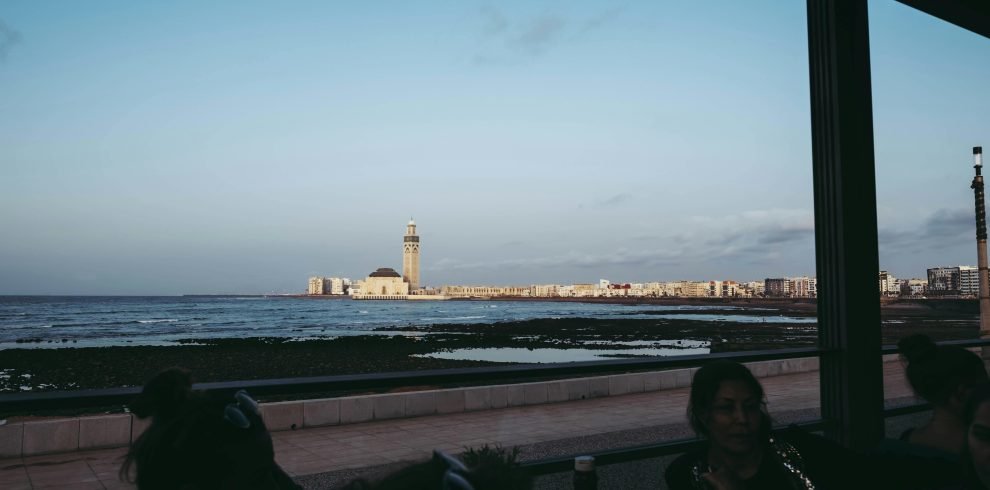 Scenic view of Hassan II Mosque from the Casablanca coastline during daytime with people in a café foreground.