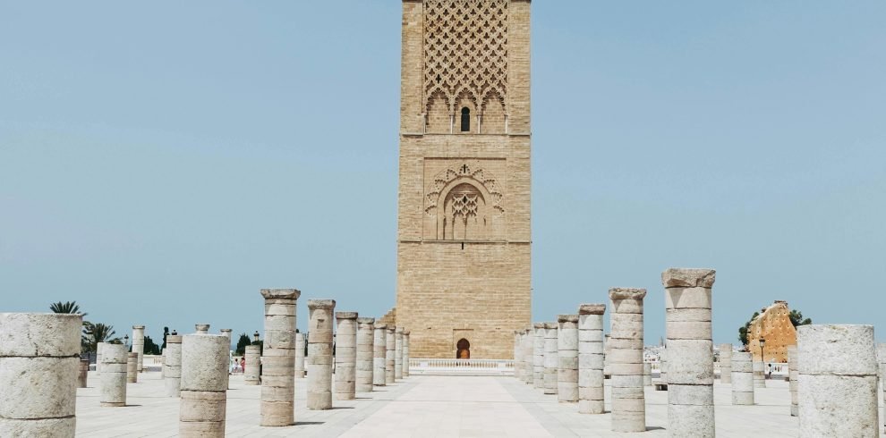 Hassan Tower in Rabat, Morocco stands tall amidst ancient columns under a clear blue sky.