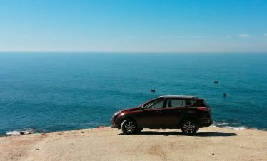 Red SUV parked on a cliff edge with a serene ocean view in Sidi Ifni, Morocco.