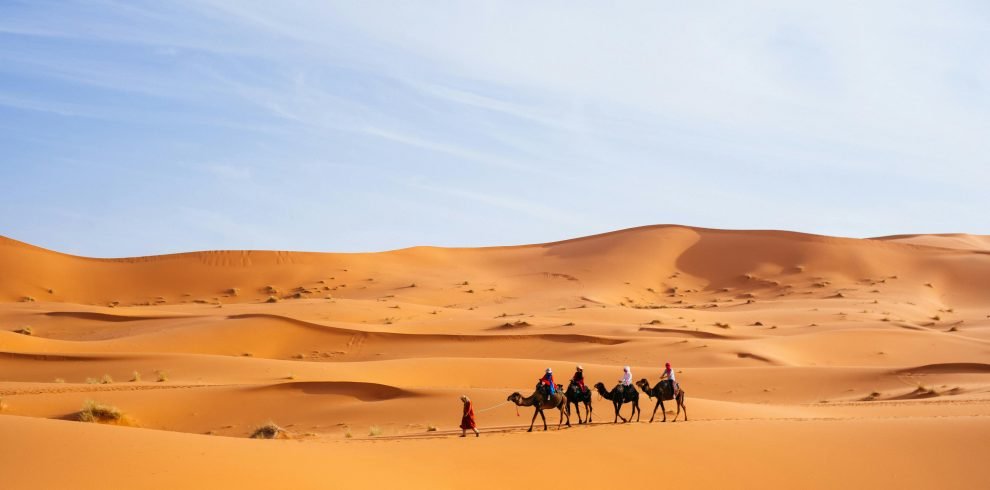 Tourists riding camels across the dunes of Merzouga, Morocco, a popular Sahara destination.