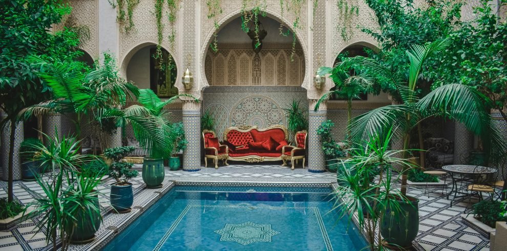 Elegant Moroccan courtyard featuring lush greenery and a decorative pool, perfect for a serene escape.